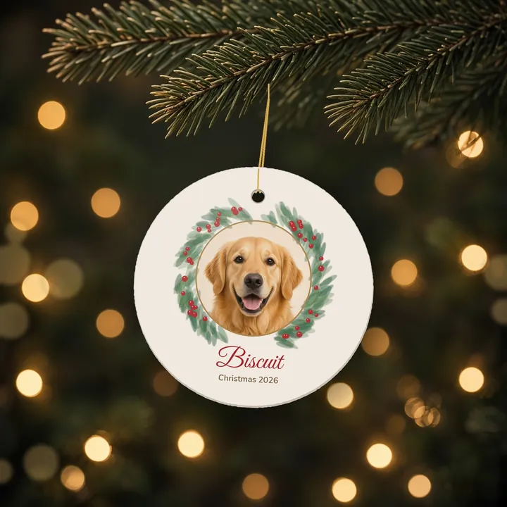 Round ceramic ornament with a golden retriever photo in a watercolor wreath, named Biscuit, hanging on a tree